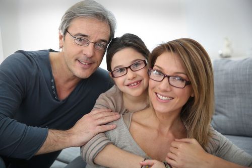 Woman smiles while holding glasses, testing her vision in an eye doctor's office.