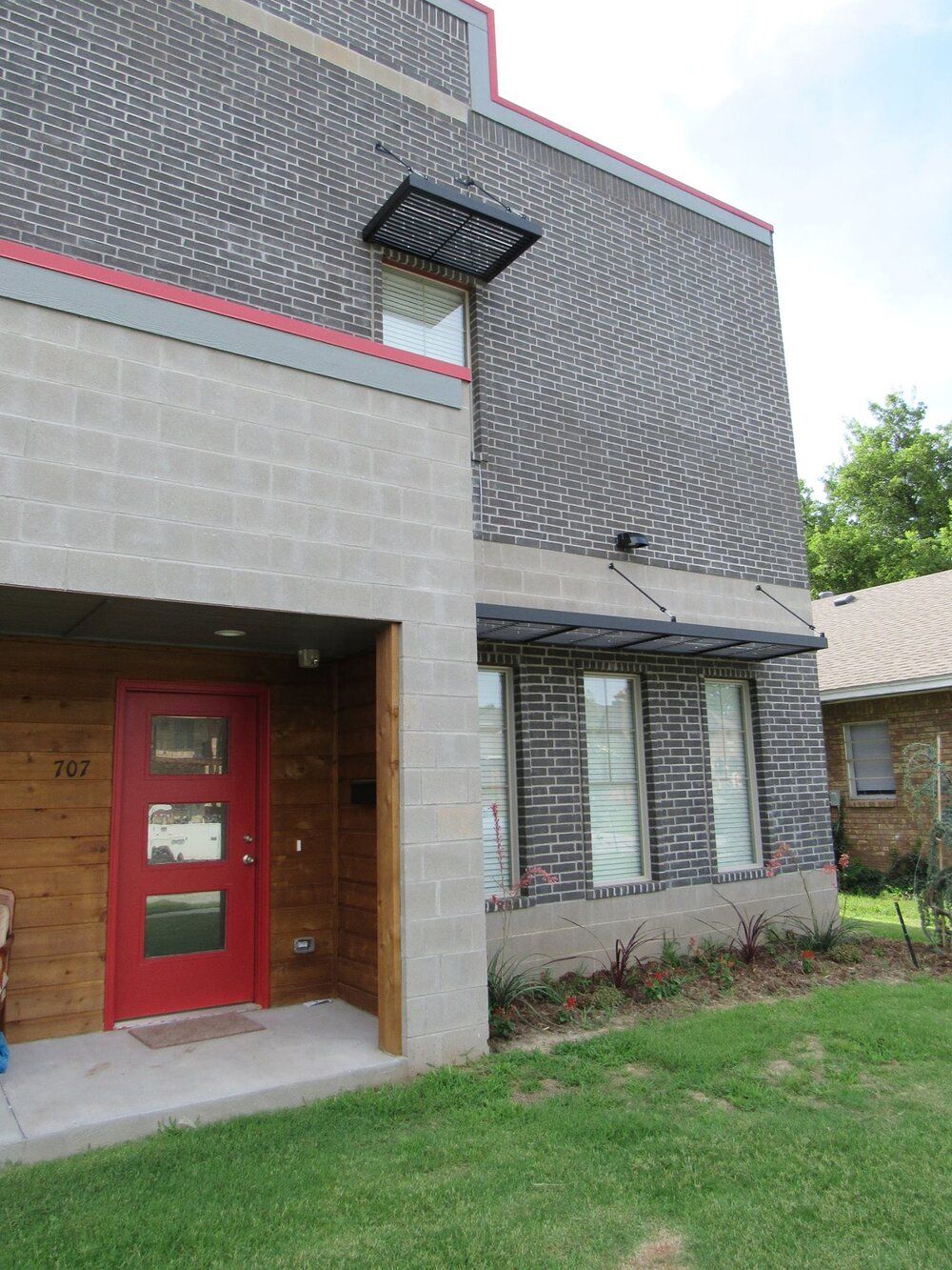 A brick building with a red door and a lawn in front of it