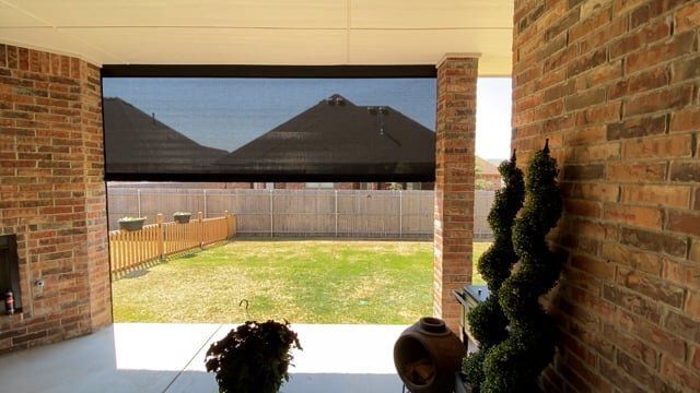 A patio with a brick wall and a black shade on it.
