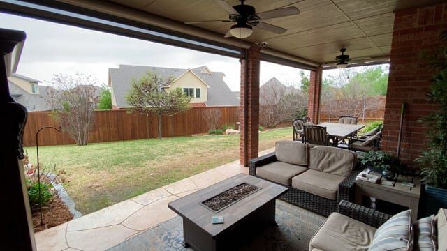 A patio with a fire pit , couch , table , chairs and a ceiling fan.