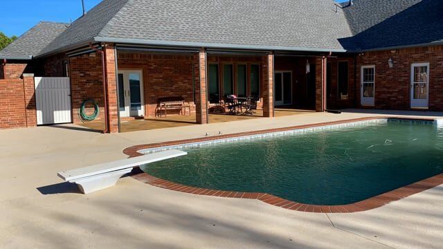 A large swimming pool is in the backyard of a brick house.
