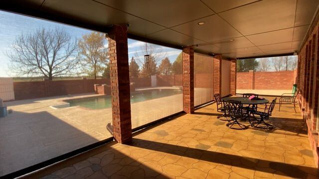 A patio with a table and chairs and a pool in the background.