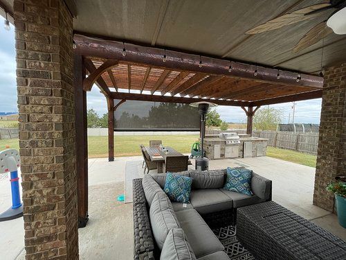 A patio with a couch , table and chairs under a pergola.