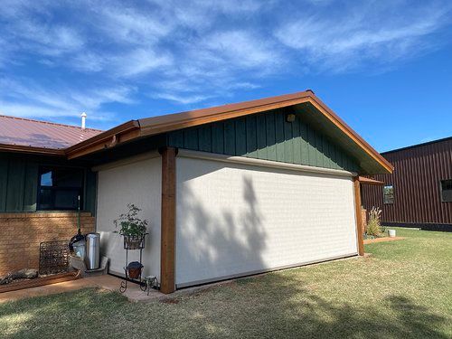 A garage with a green roof and a white door is in the backyard of a house.