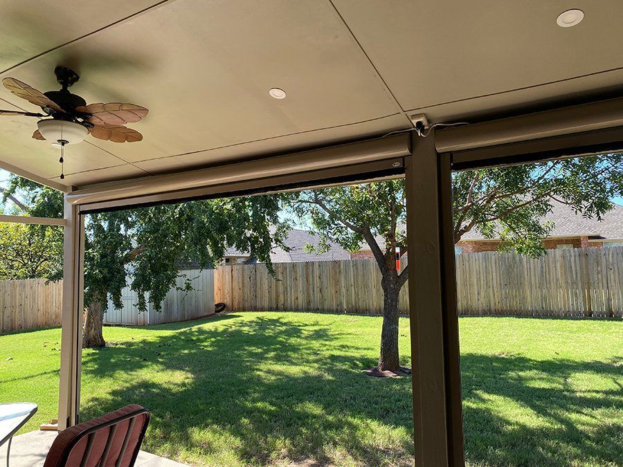 A screened in porch with a ceiling fan and a view of a backyard.