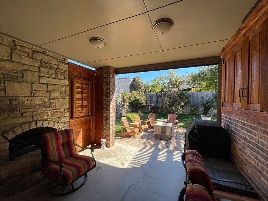 A patio with rocking chairs , a table and a grill.