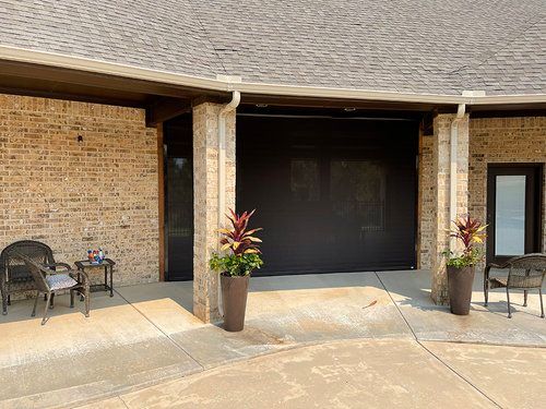 A brick house with a black garage door and potted plants in front of it.