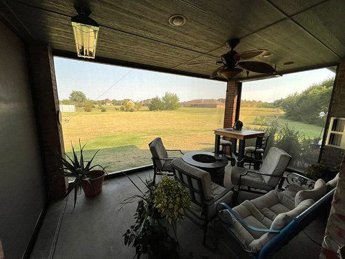 A screened in porch with a view of a field and a ceiling fan.