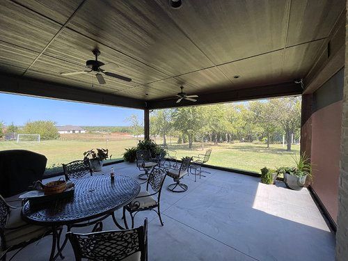 A screened in porch with a table and chairs and a ceiling fan.