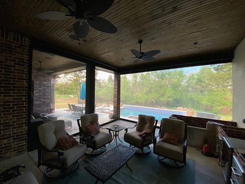 A screened in porch with rocking chairs , a couch , a table and a ceiling fan.