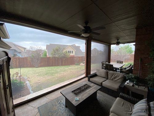A screened in porch with a couch , table , chairs and a ceiling fan.