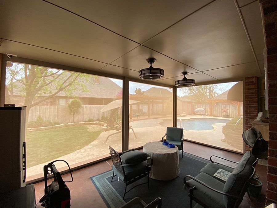 A screened in porch with chairs , a table and a ceiling fan.
