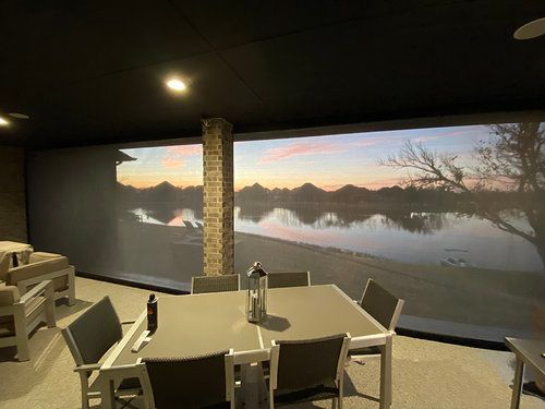 A dining room with a table and chairs and a large screen on the wall.