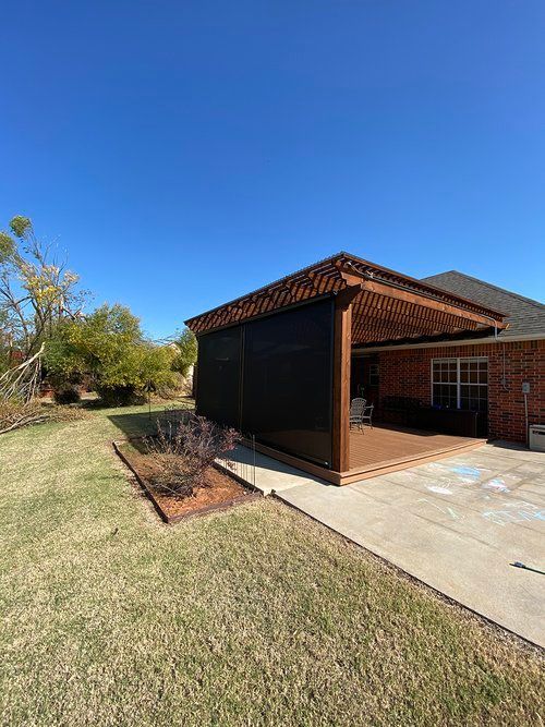 A patio with a screened in porch and a brick house in the background.