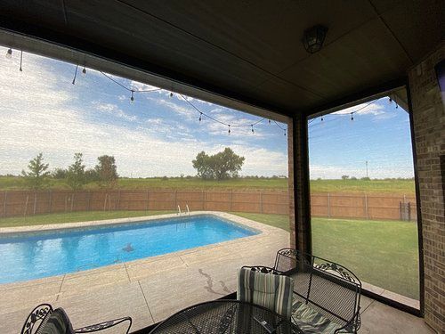 A screened in porch with a swimming pool in the background.