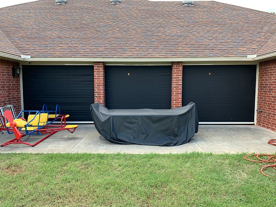 A couch is covered in a black cover in front of a garage door.