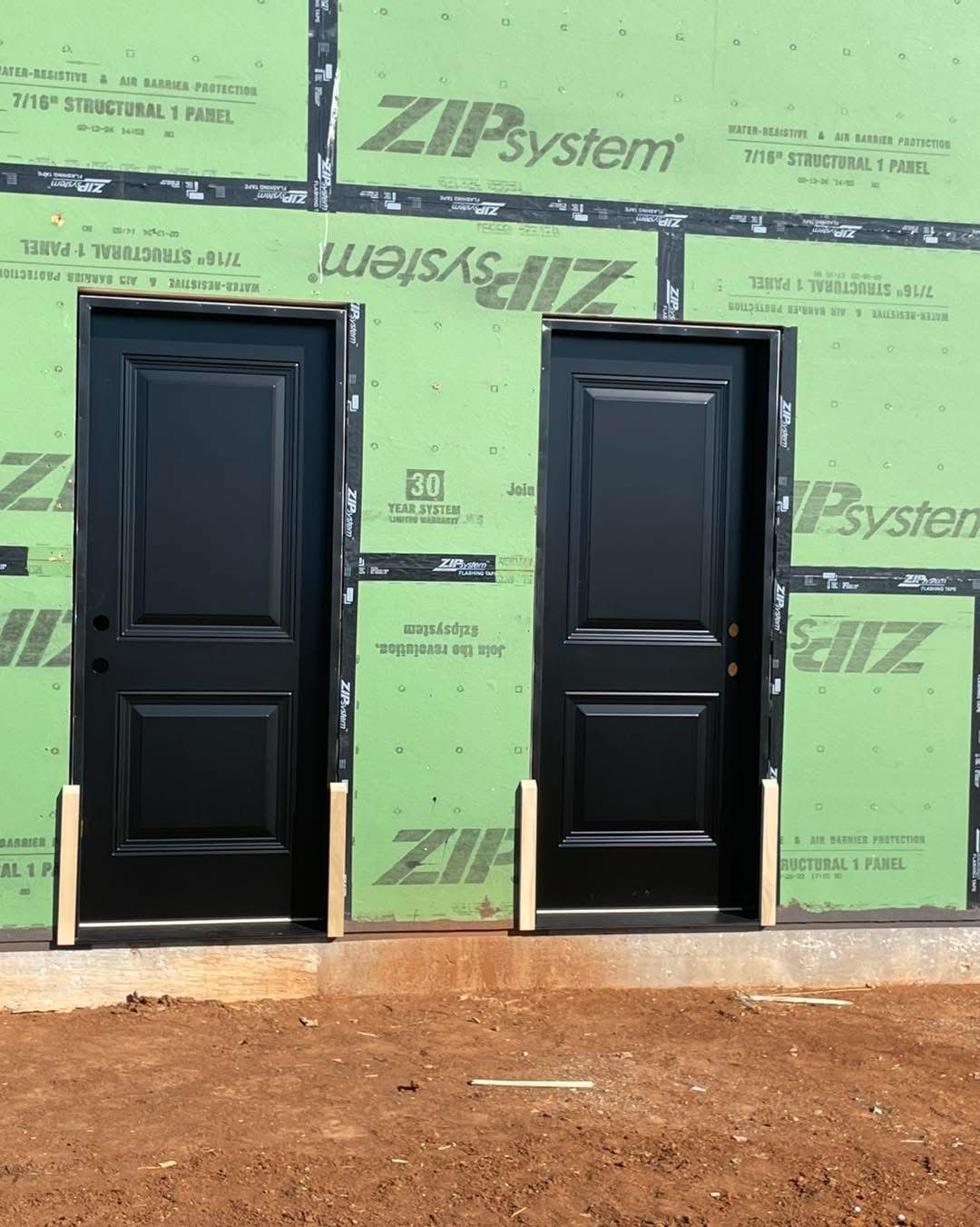 Two black exterior doors installed on a building under construction, green insulation visible.