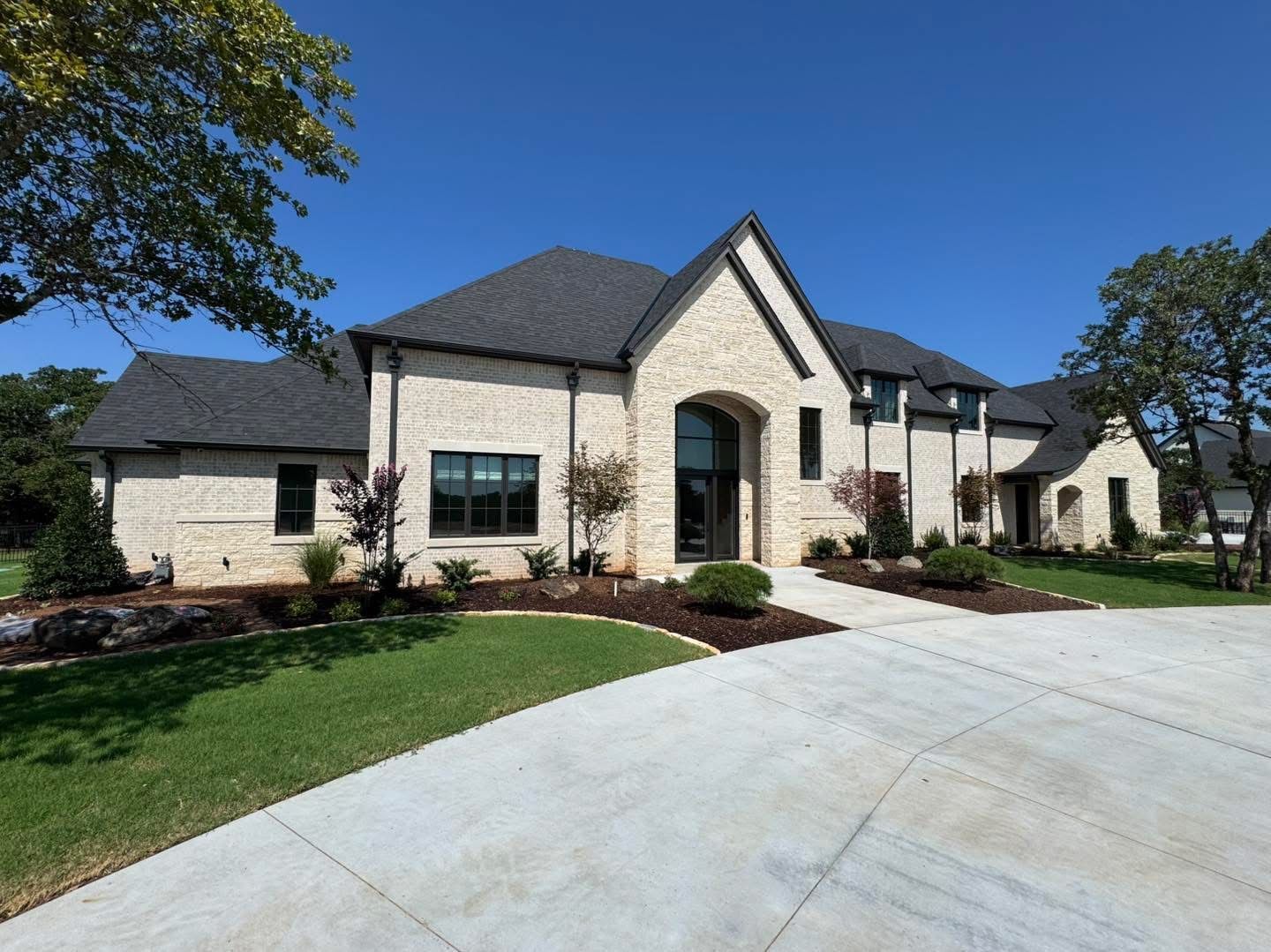 Modern beige brick house with dark roof, arched entryway, and concrete driveway.