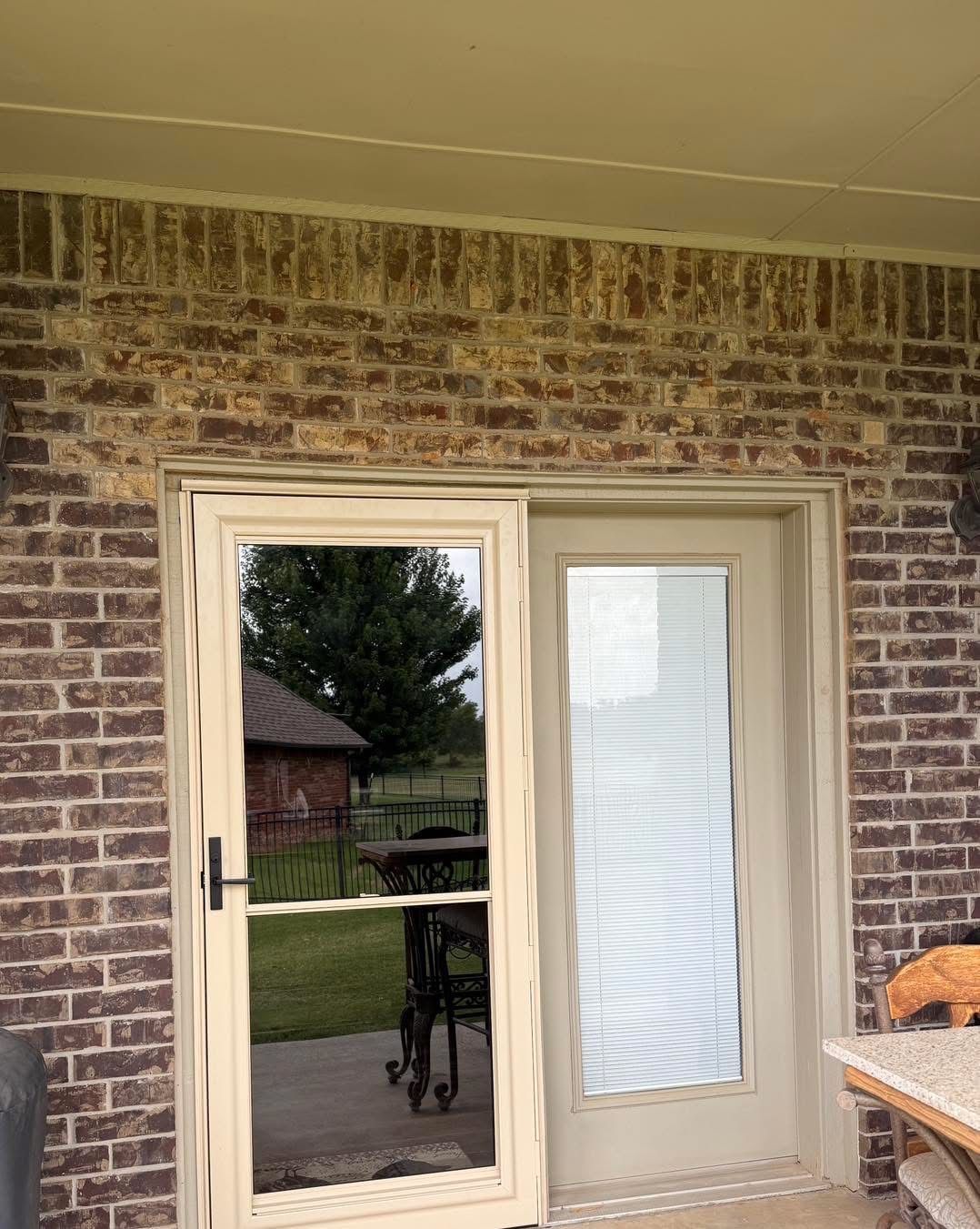 Brick exterior with tan framed door and screen door. View of yard through glass.