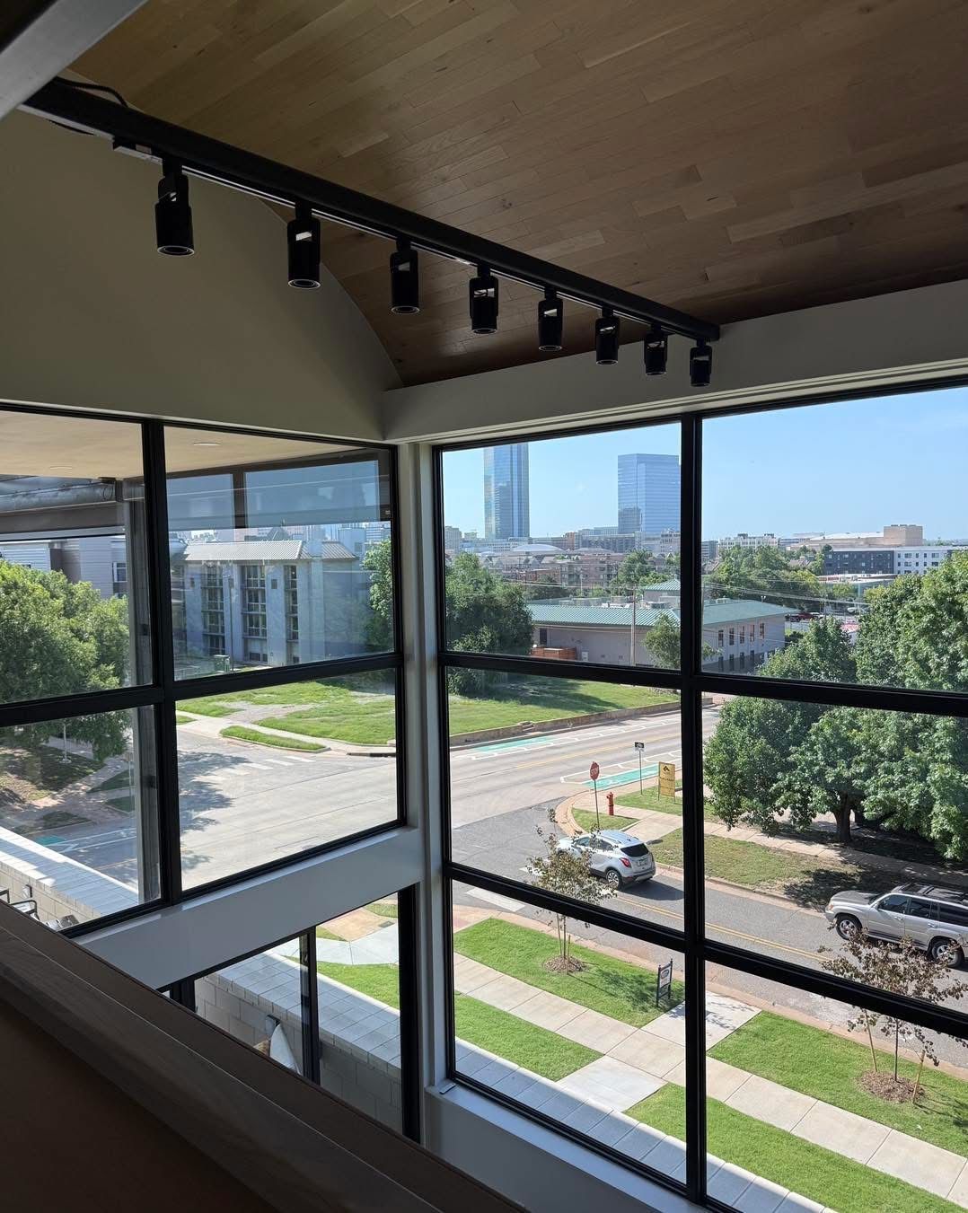 View from an interior window, overlooking a city street and buildings; black track lighting on ceiling.