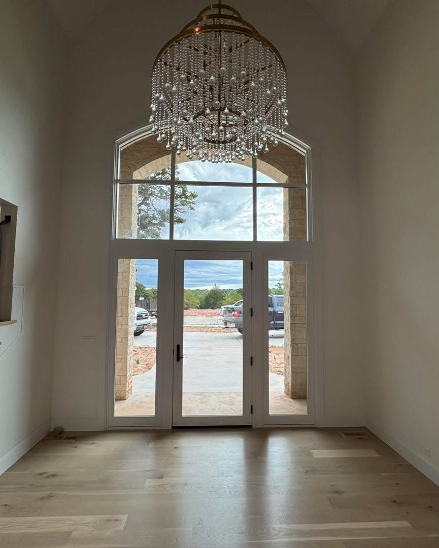 A large, bright entryway with a chandelier, glass doors, and a view of construction outside.