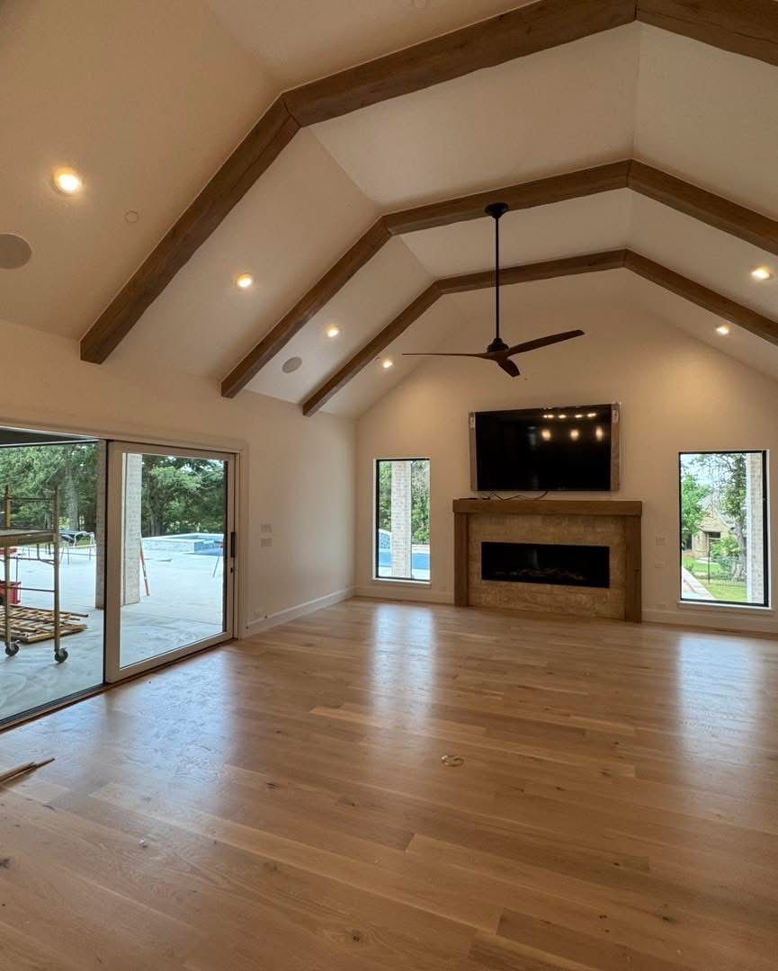 Spacious living room with vaulted ceiling, wooden beams, and fireplace. Hardwood floors and sliding glass door.
