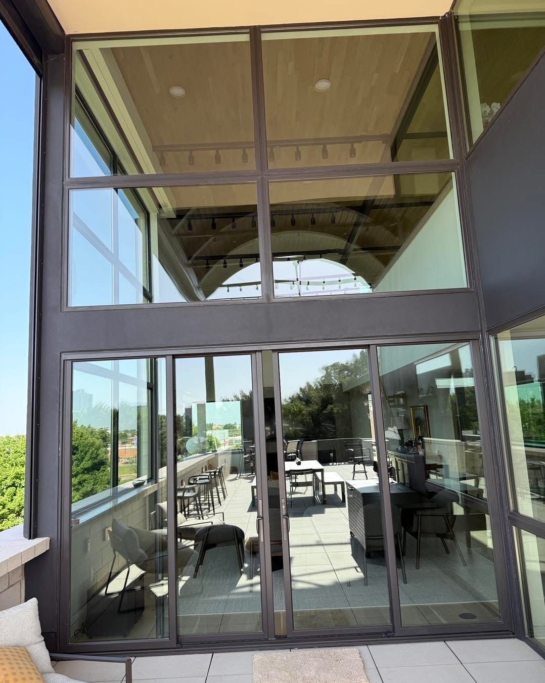 Glass doors leading to a patio with furniture. Modern building with large windows. Blue sky.