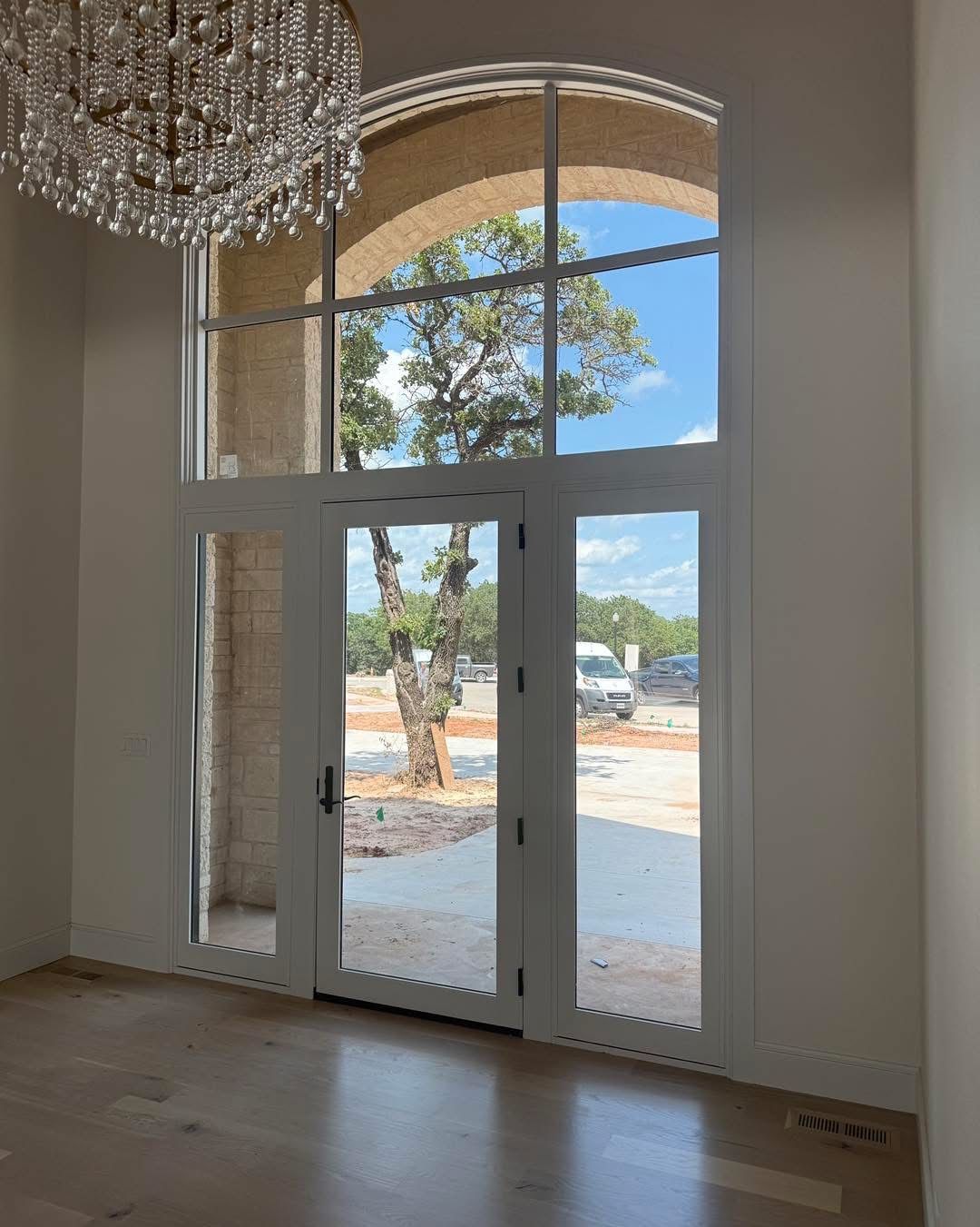 Tall arched doorway with glass windows and doors, chandelier, view of tree and sky.