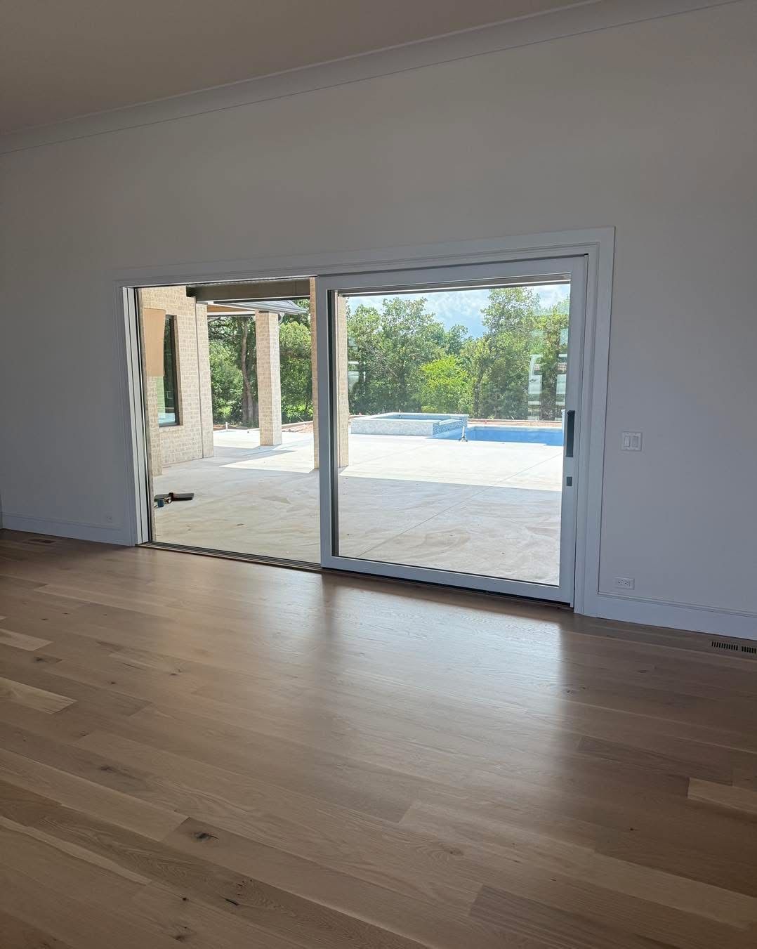 Wooden floored room with sliding glass door to a patio and pool.