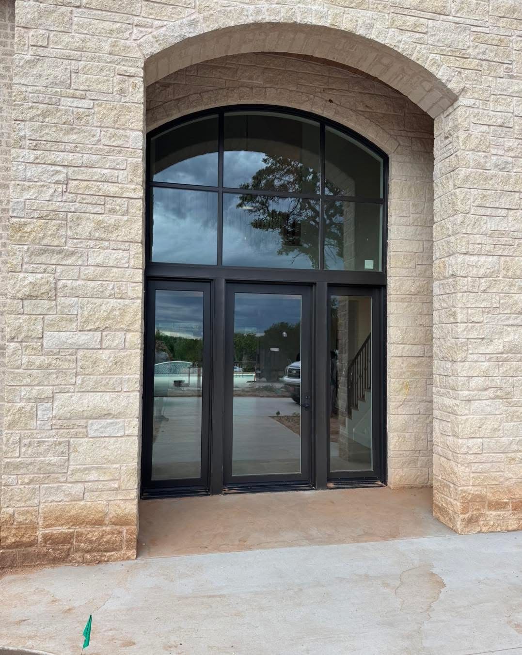 Exterior doorway with arched top and glass panels, set in light-colored stone. Black trim, reflecting sky and surroundings.