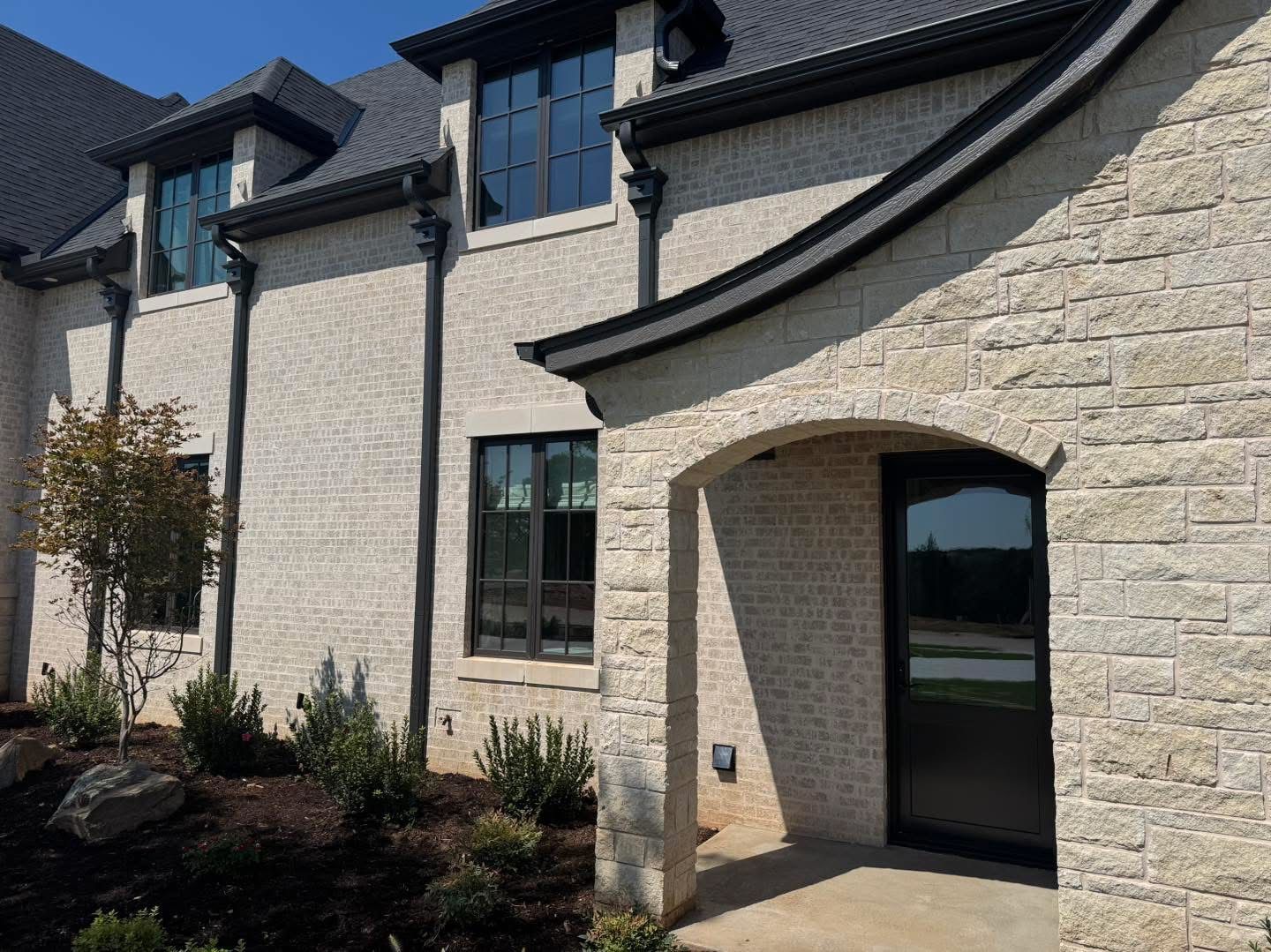 Beige brick home with black windows and roof, a curved entrance.