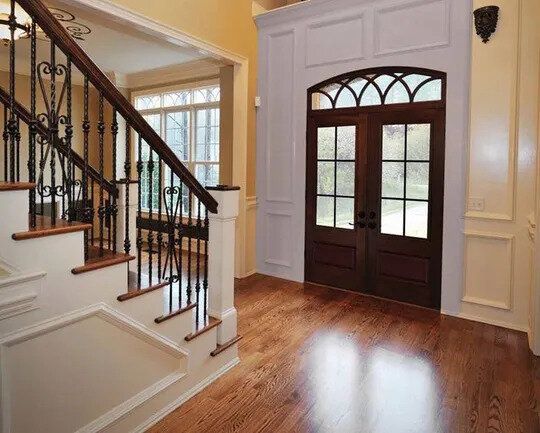 A hallway with hardwood floors , stairs , and a double door.