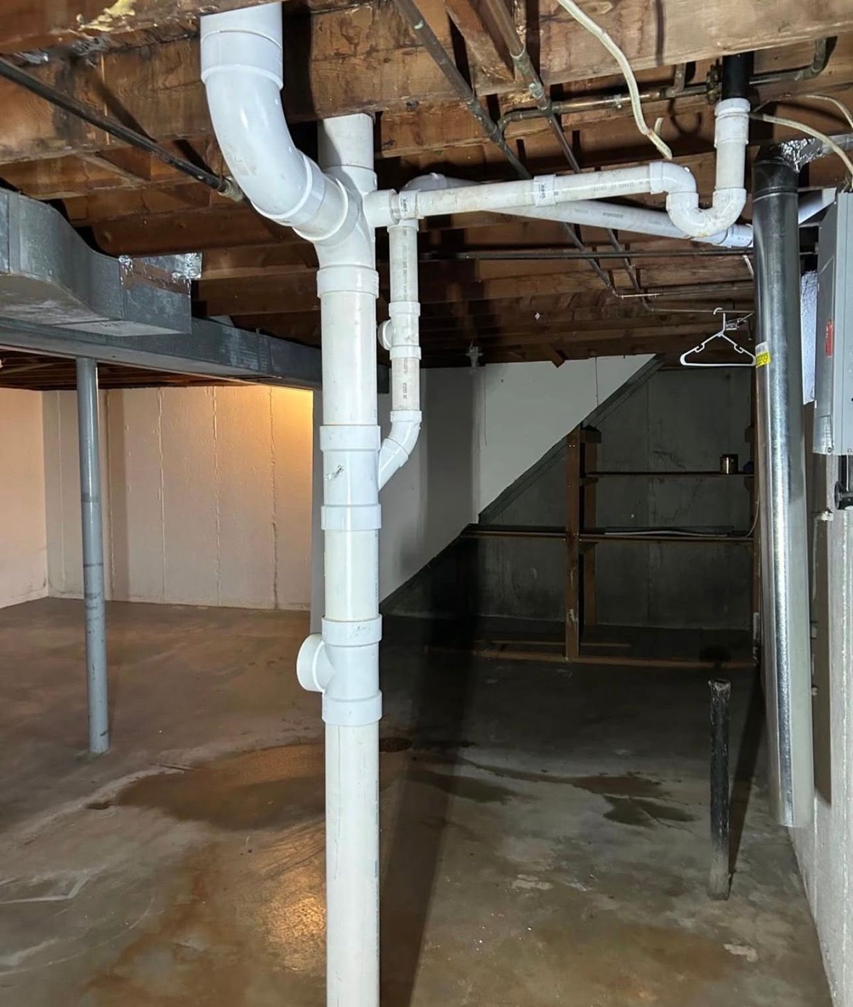 White PVC pipes installed in a basement ceiling, with a dark staircase and a concrete floor.