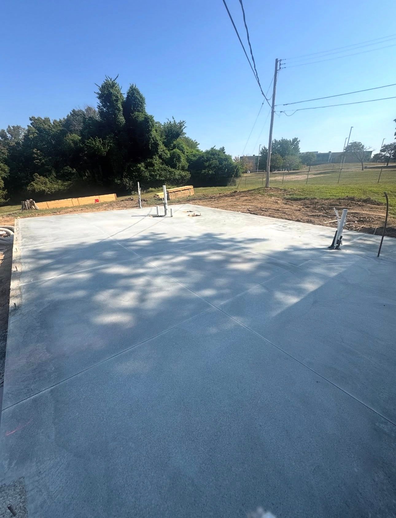 Freshly poured concrete slab in an open, sunny area. Electrical lines and trees are visible in the background.