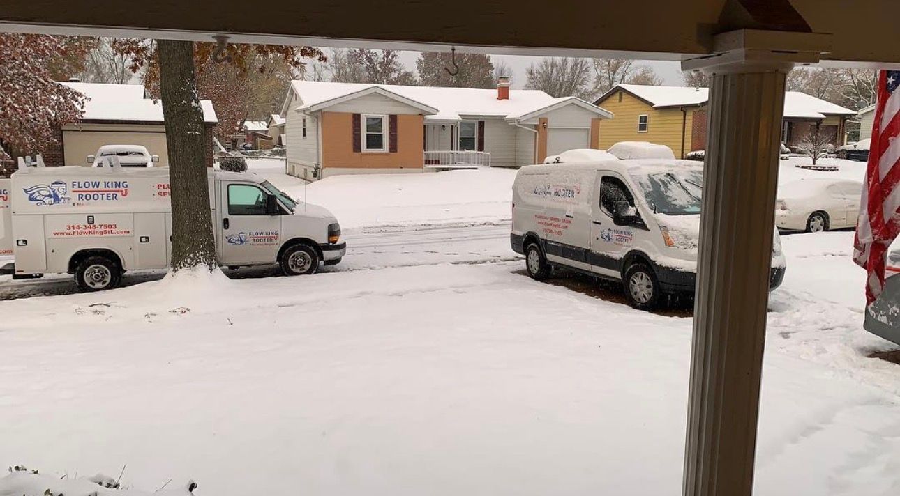 Snow-covered residential street with service vans parked in front.
