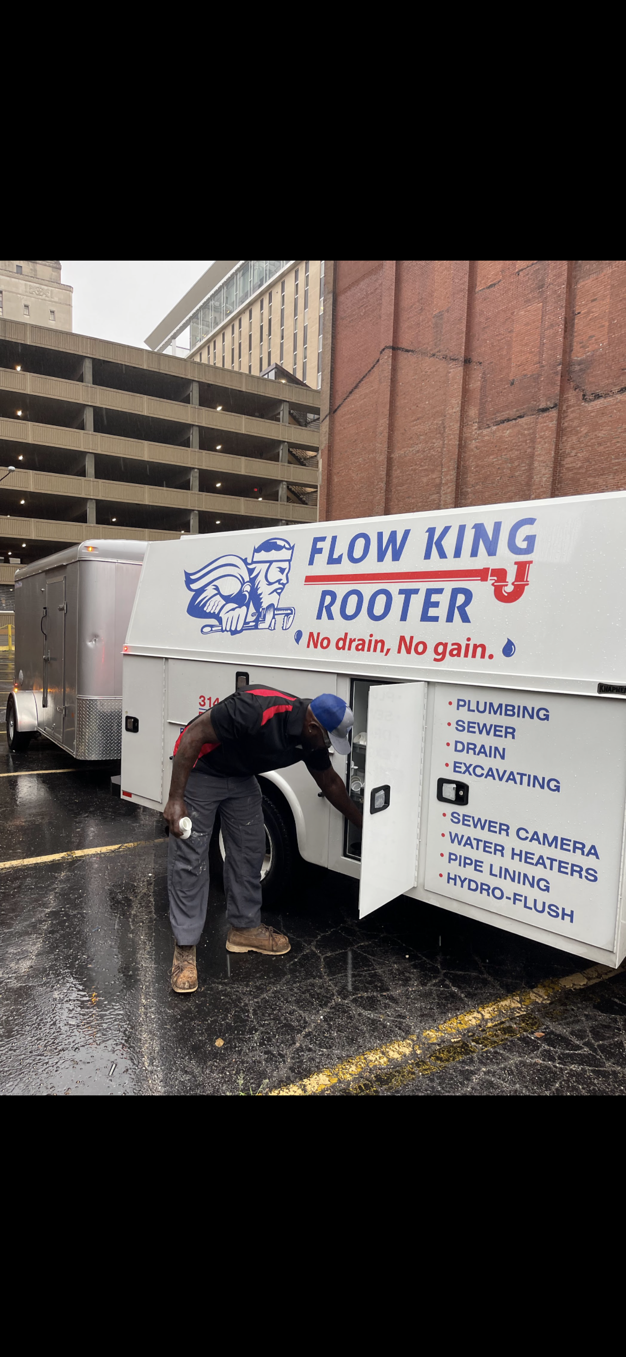 A person wearing dark work clothes is working at a Flow King Rooter truck, in a parking lot.