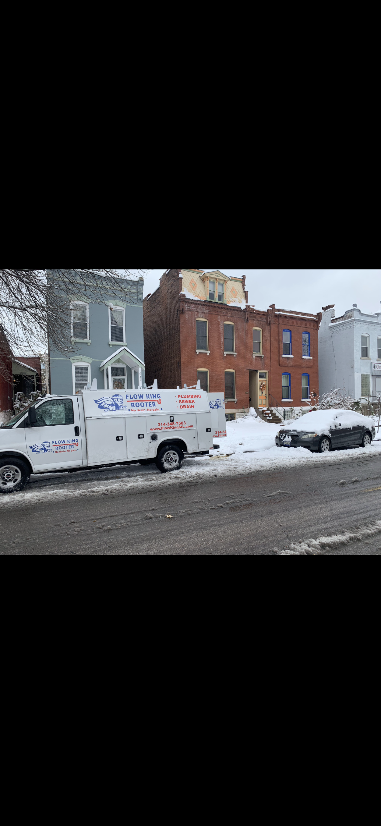 A white service truck parked on a snow-covered street in front of row houses.