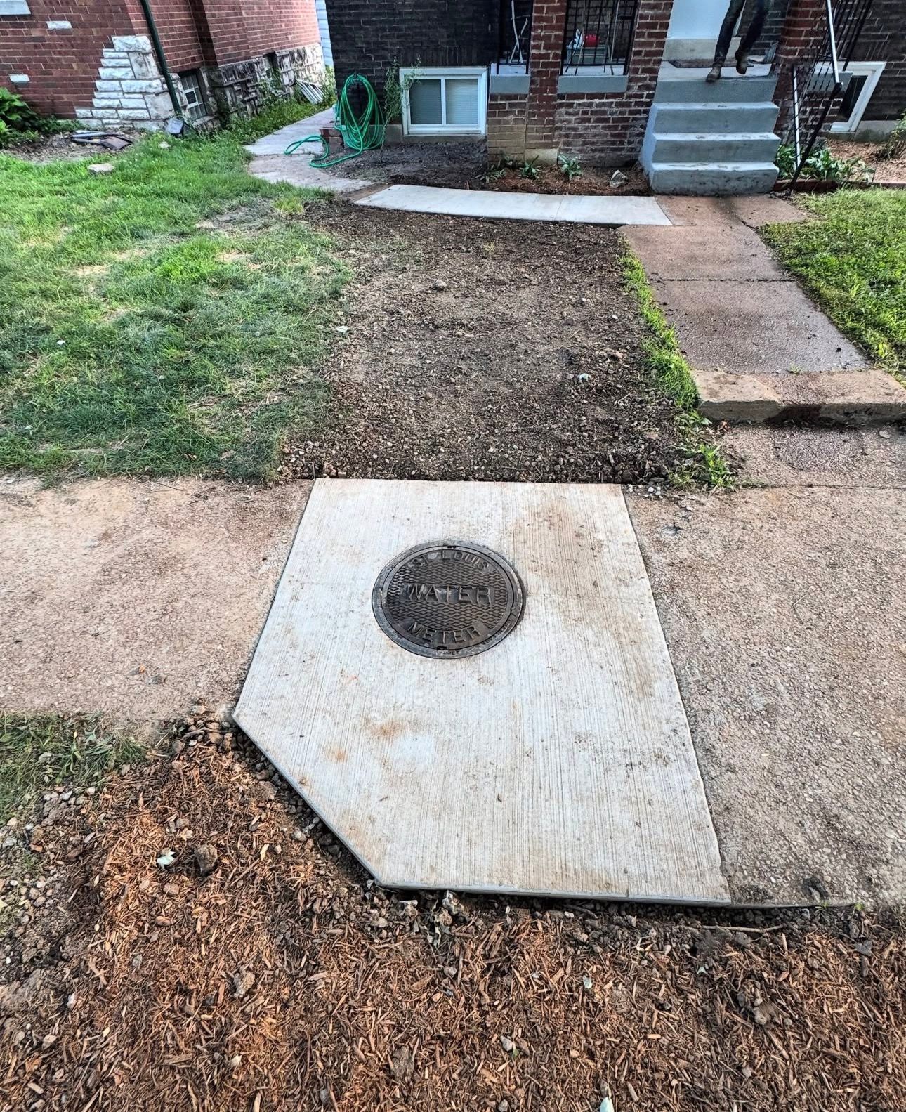 Concrete sidewalk with a utility access point, and brown mulch.