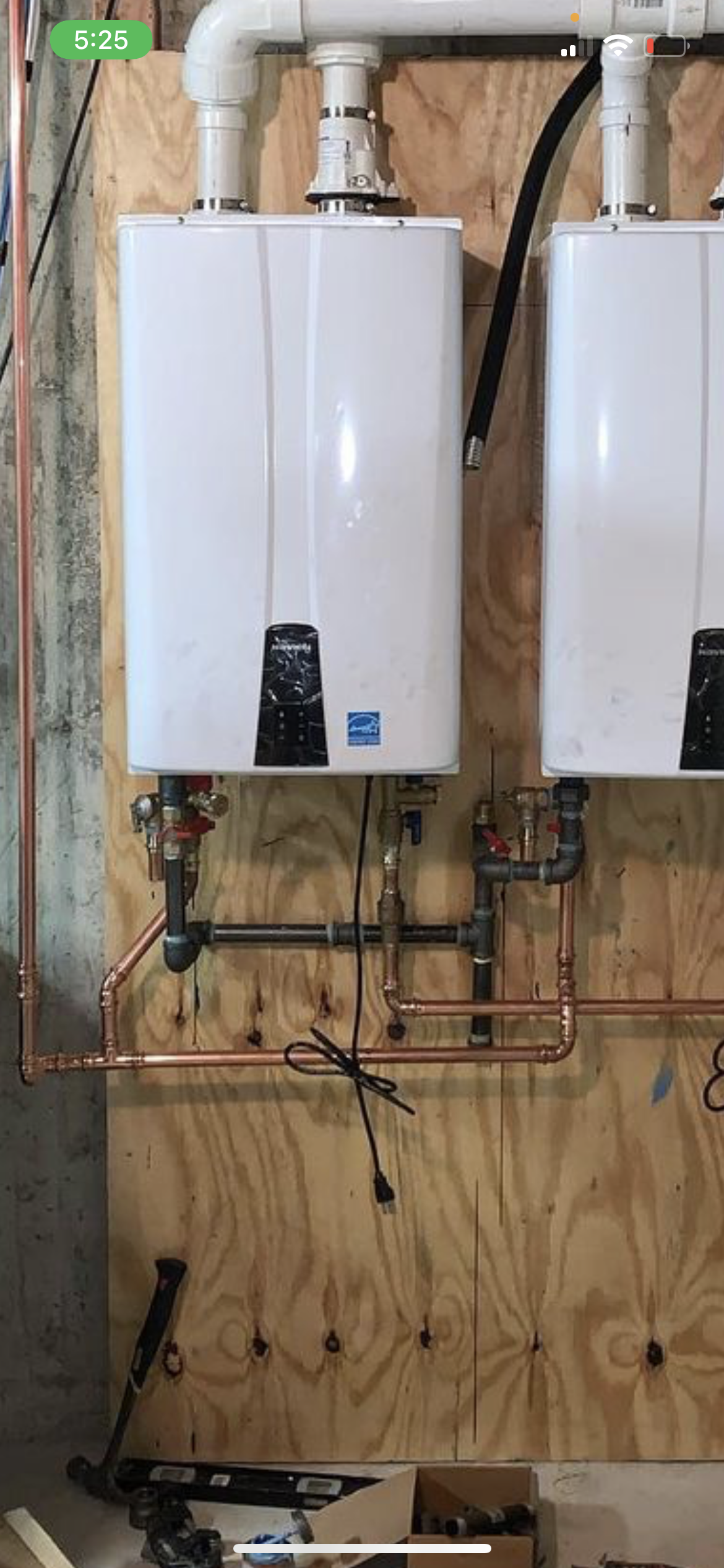 Two white water heaters mounted on plywood with copper pipes.