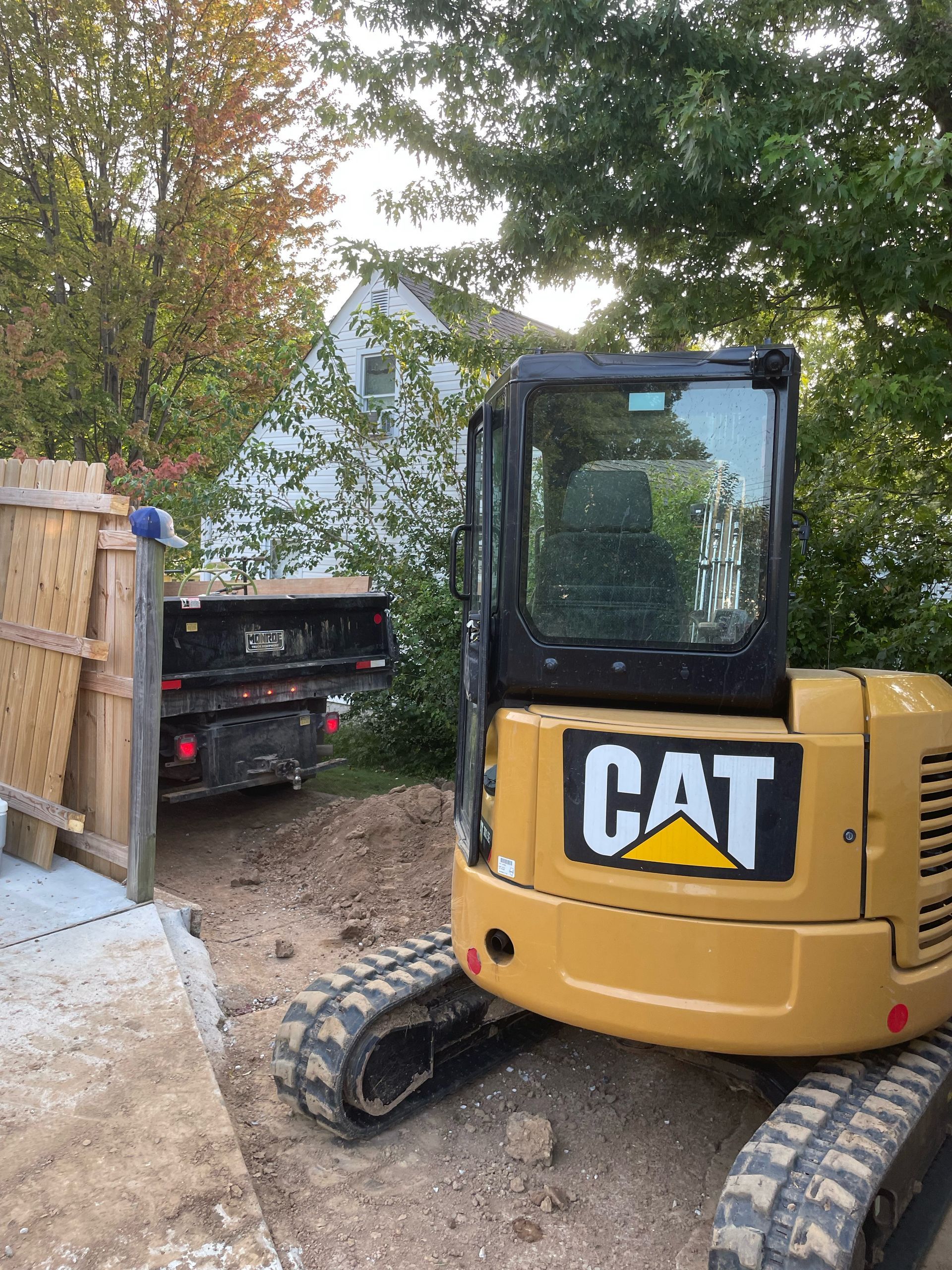 Yellow CAT excavator next to a truck on a construction site near a house.