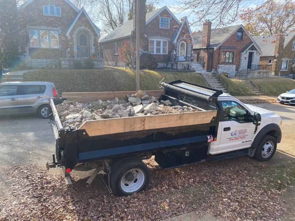 White dump truck filled with debris parked on a street with houses in the background.