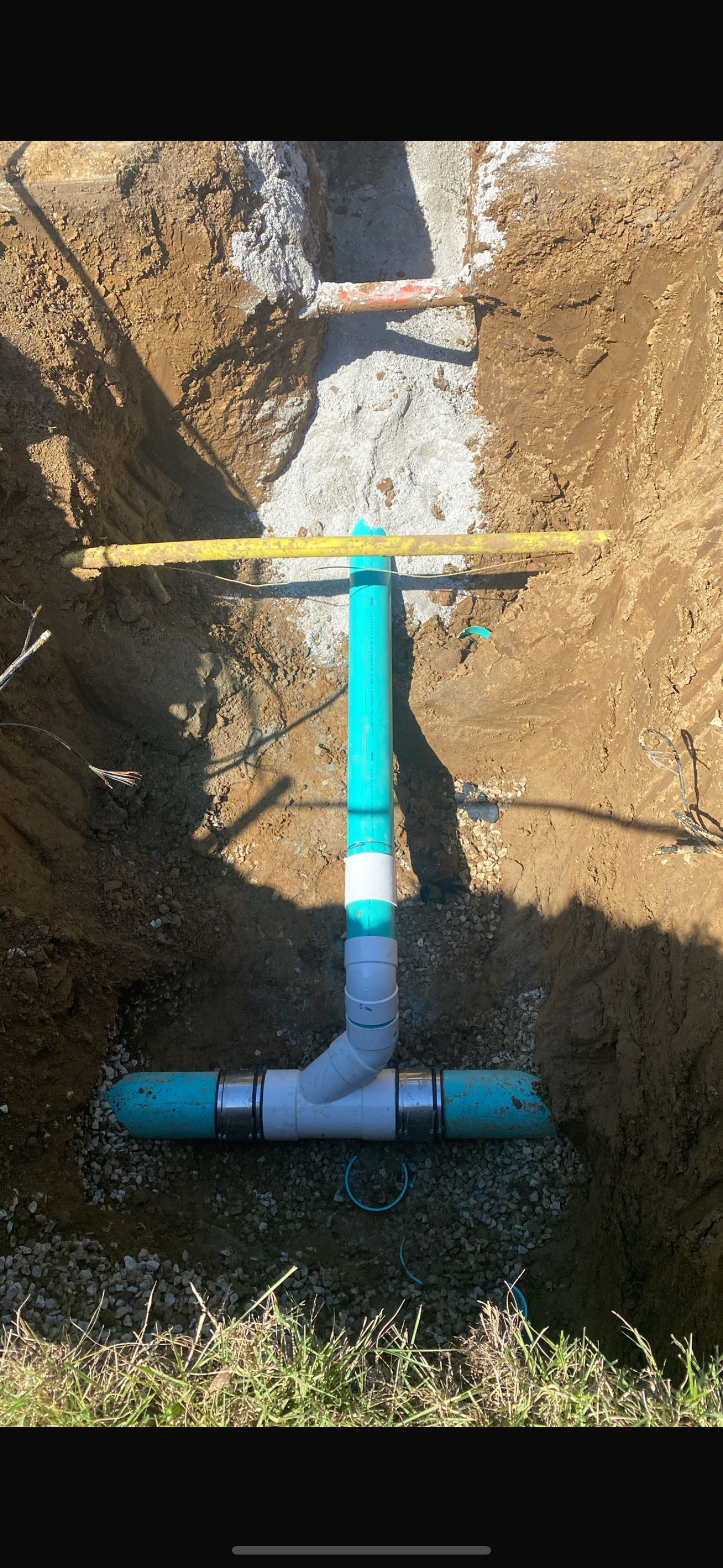 Plumbing: PVC pipes in a trench, connected by fittings. Yellow level tool spans pipes.