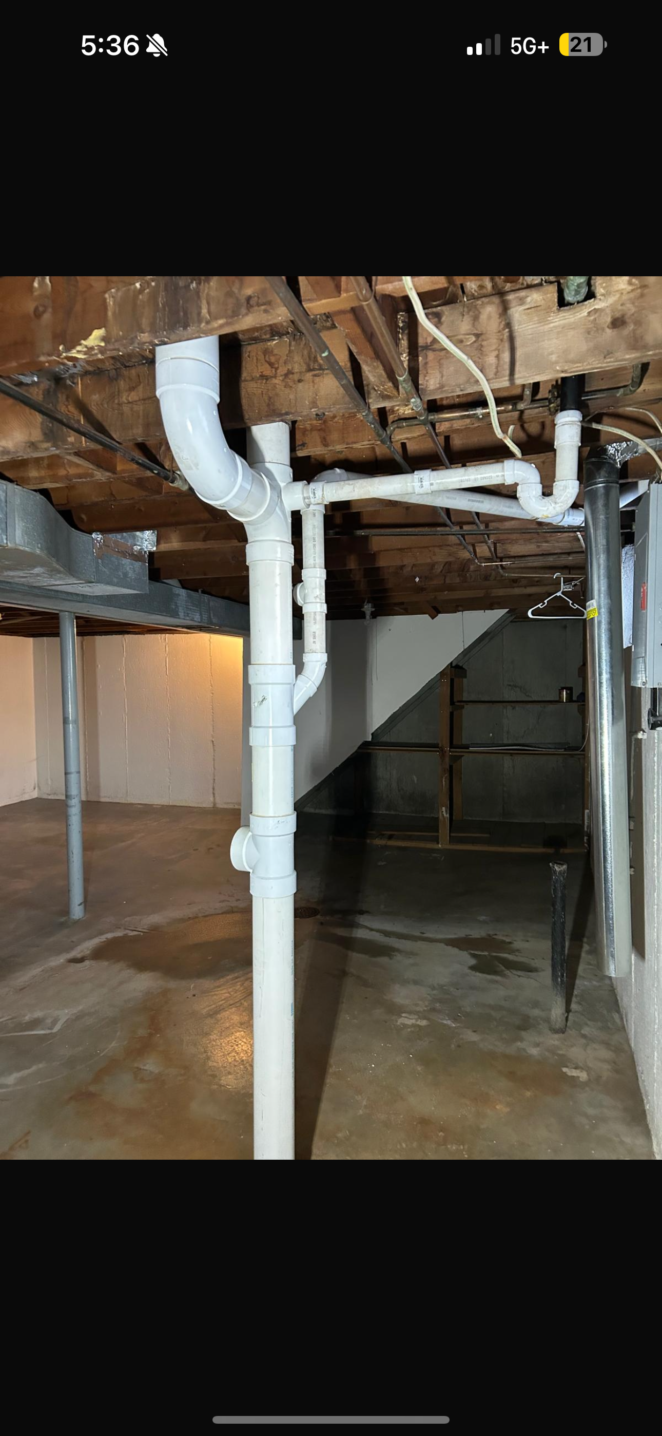 Basement plumbing system with white pipes near wooden ceiling and concrete floor.