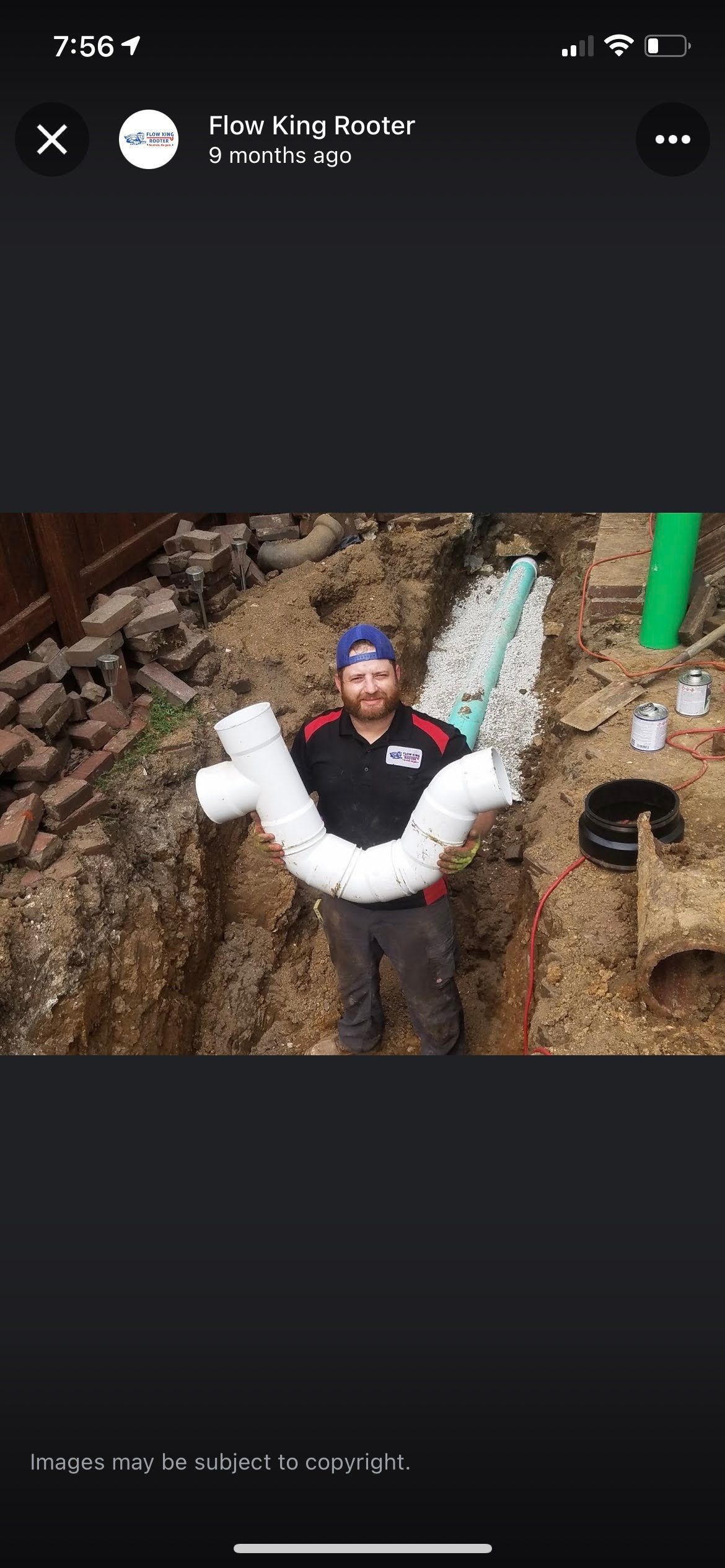 Plumber holding a white PVC pipe in a trench, ready to install, outside.