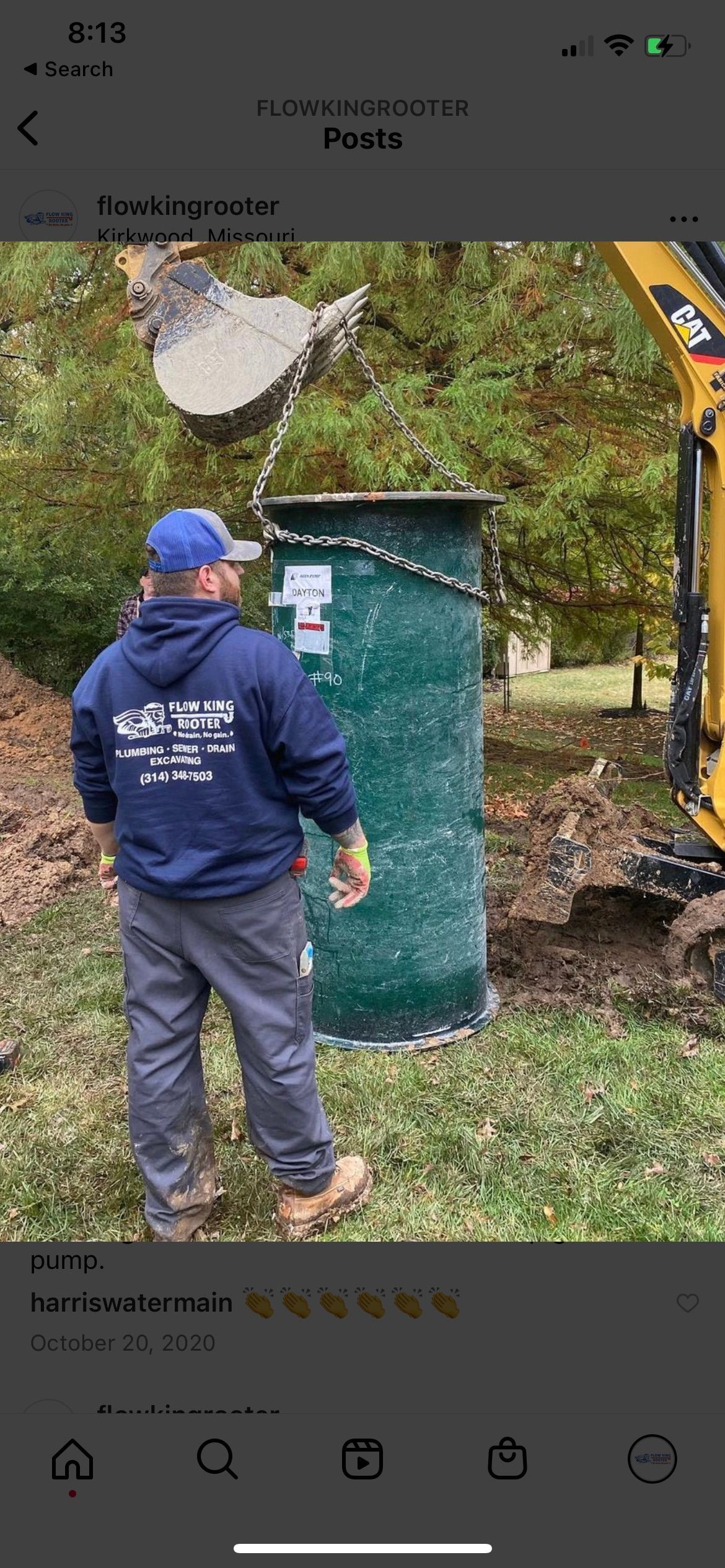 A worker watching a green septic tank being lifted by a small excavator in a yard.
