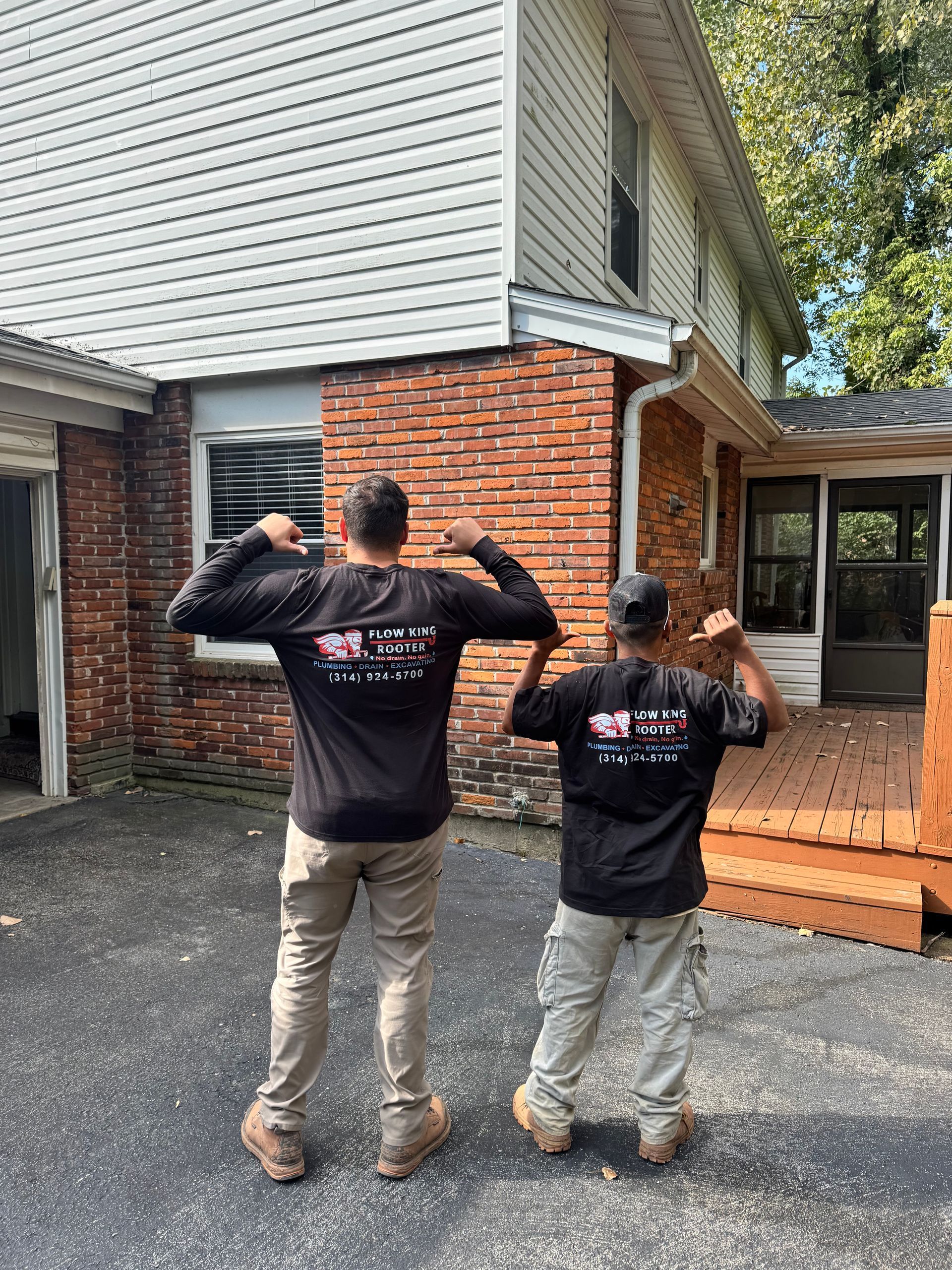 Two people flex arm muscles in front of a house with a wooden deck.