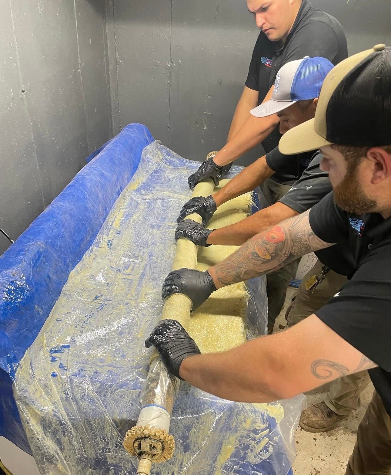Three people wearing gloves working on a large cylinder, likely for industrial repair.