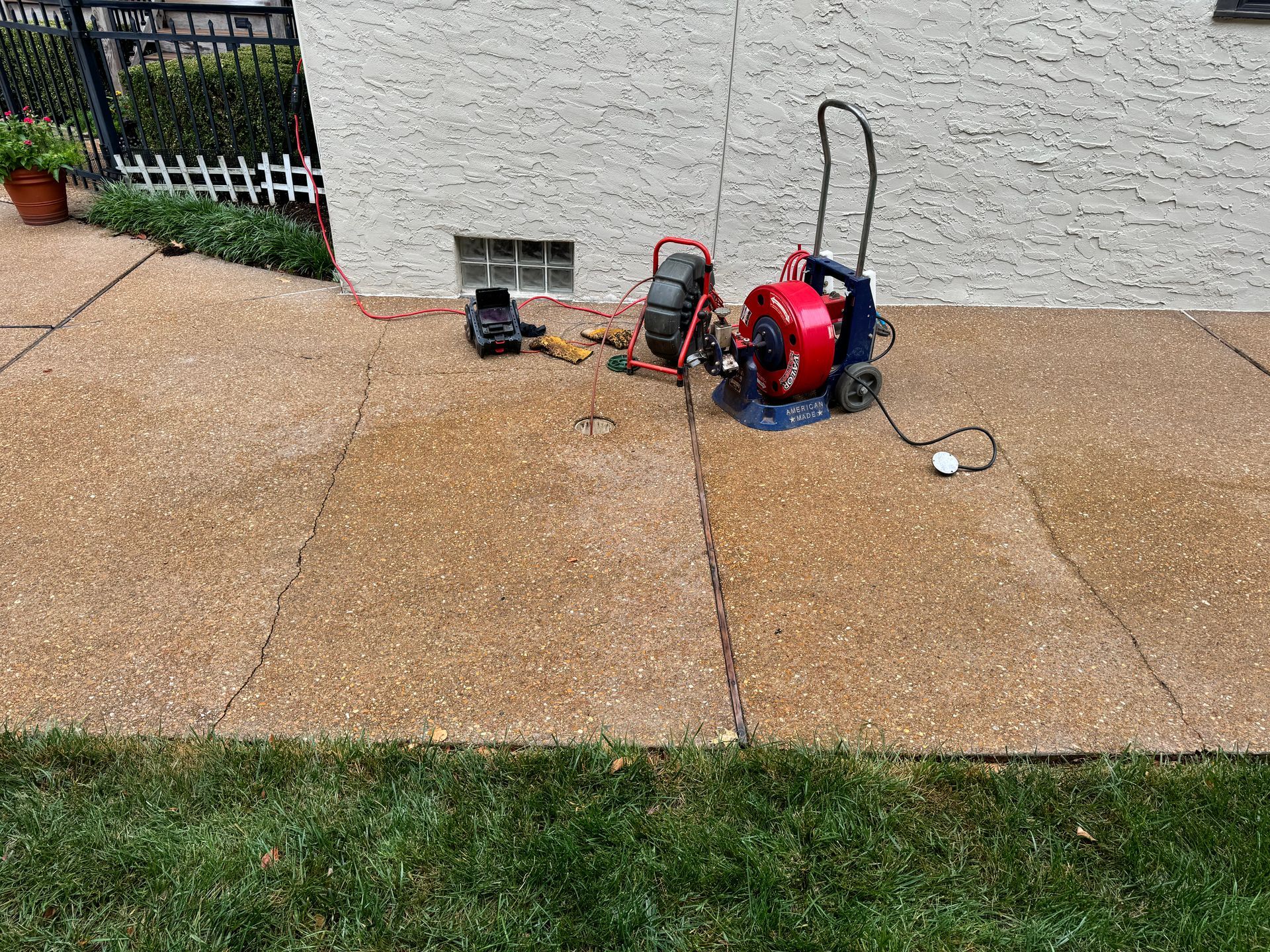Plumbing equipment on concrete near a house, including a cable machine and camera.