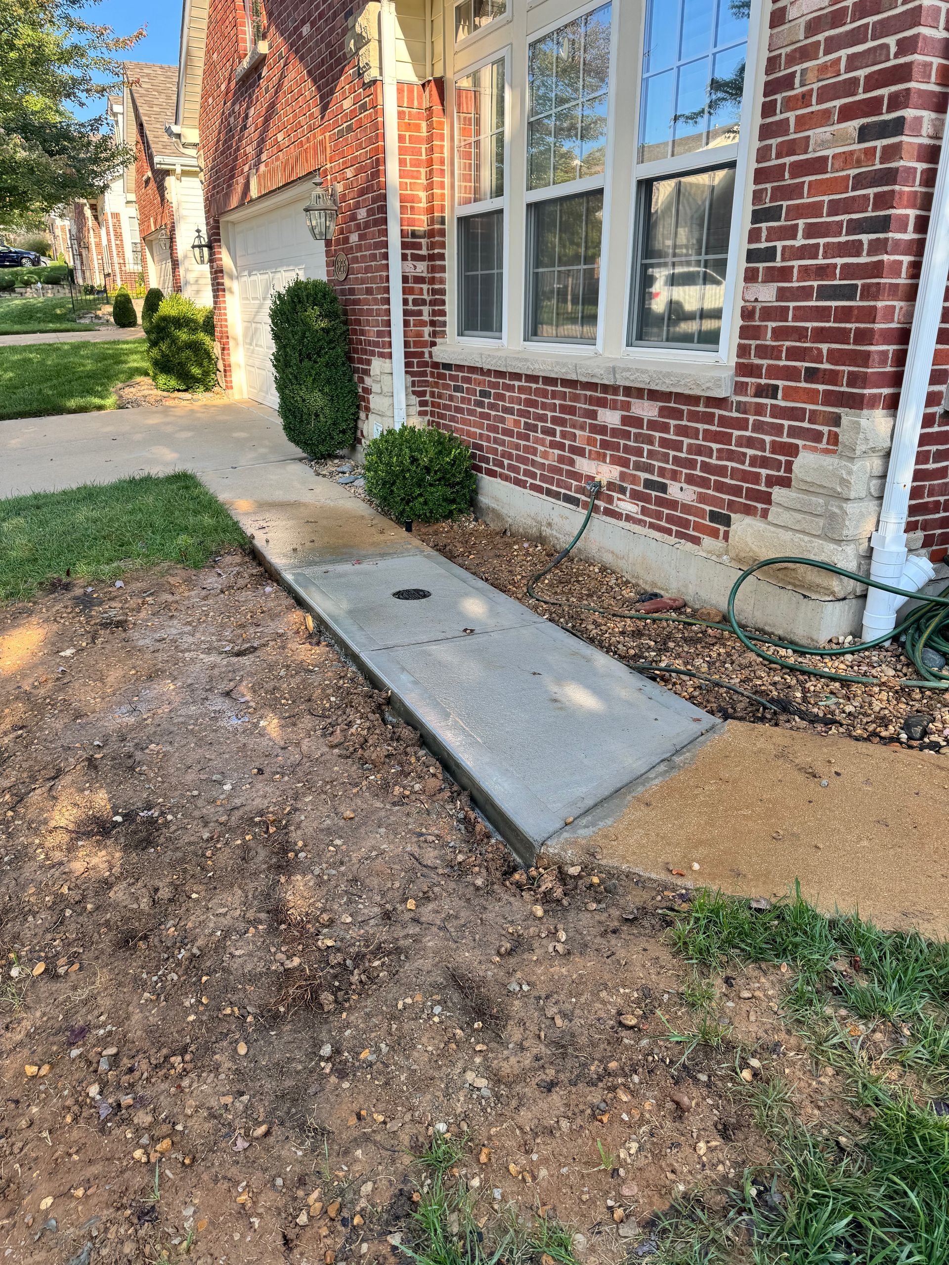 Concrete ramp leading to a brick house entrance. The area is partly dirt and grass.