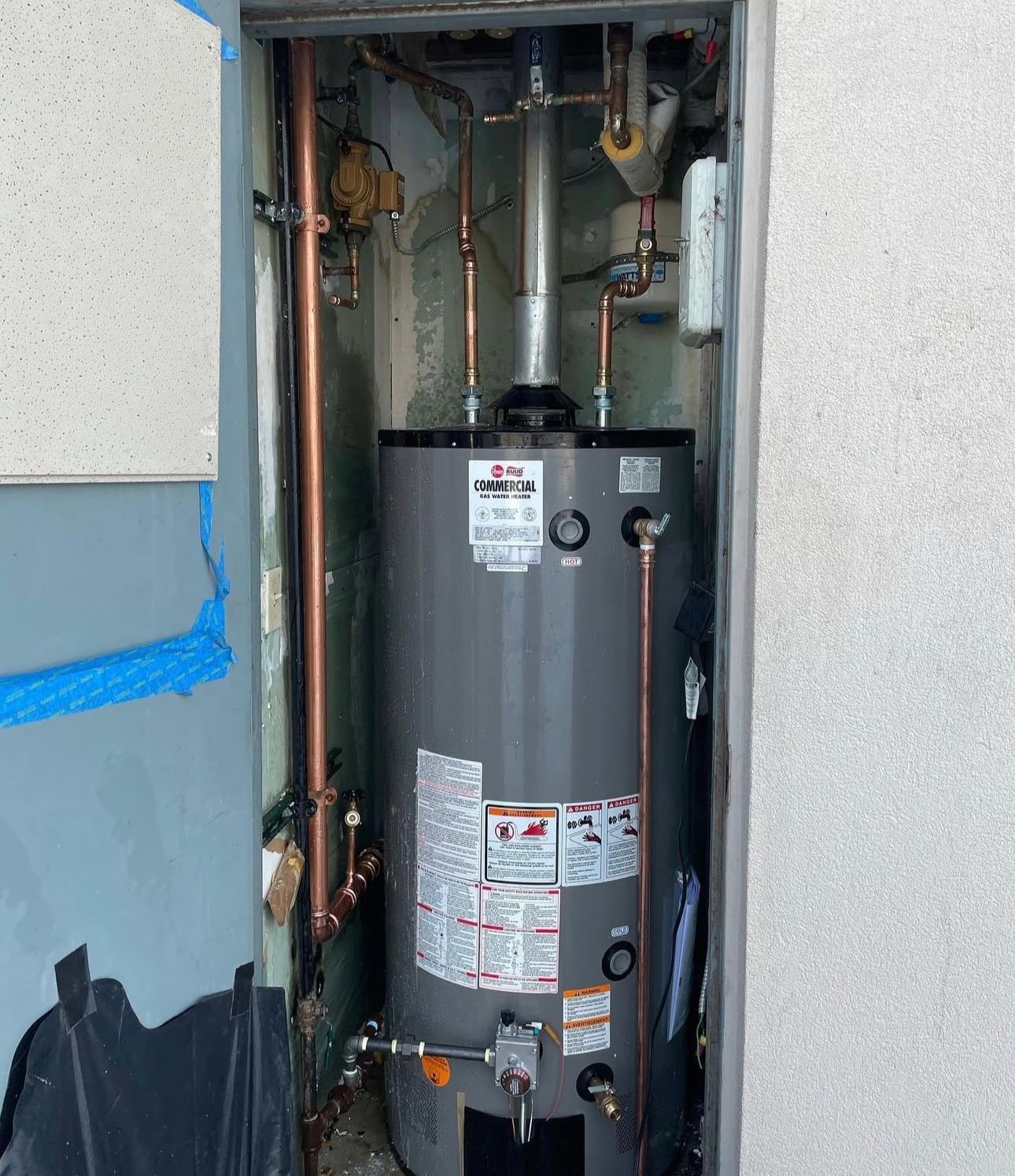 A water heater installed in a narrow alcove. Copper pipes and a metal flue are visible.